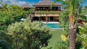 Uma casa de dois andares com piscina, rodeada por vegetação exuberante.