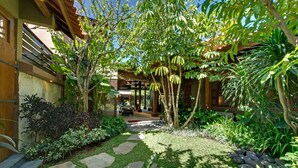 Um jardim com um caminho de pedra, diversas plantas e um edifício com fachada de madeira e grandes janelas.