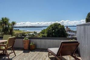 A wooden deck with two chairs and a table, overlooking a body of water with a distant island and a church. - Lakeside City Apartments - Penthouse (Rotorua)