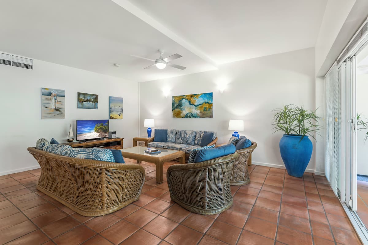 A living room with wicker furniture, a flat-screen TV, and artwork on the walls.
