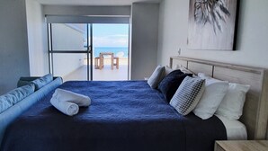 Quarto com uma cama grande, vista para a praia e um quadro na parede.