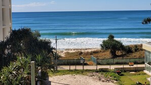 Vista para a praia com areia, ondas do oceano e uma cerca com um letreiro.