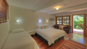 Een slaapkamer met twee bedden, een tafeltje, twee fauteuils, een raam met zonwering, en een deur die uitkomt op een tuin.