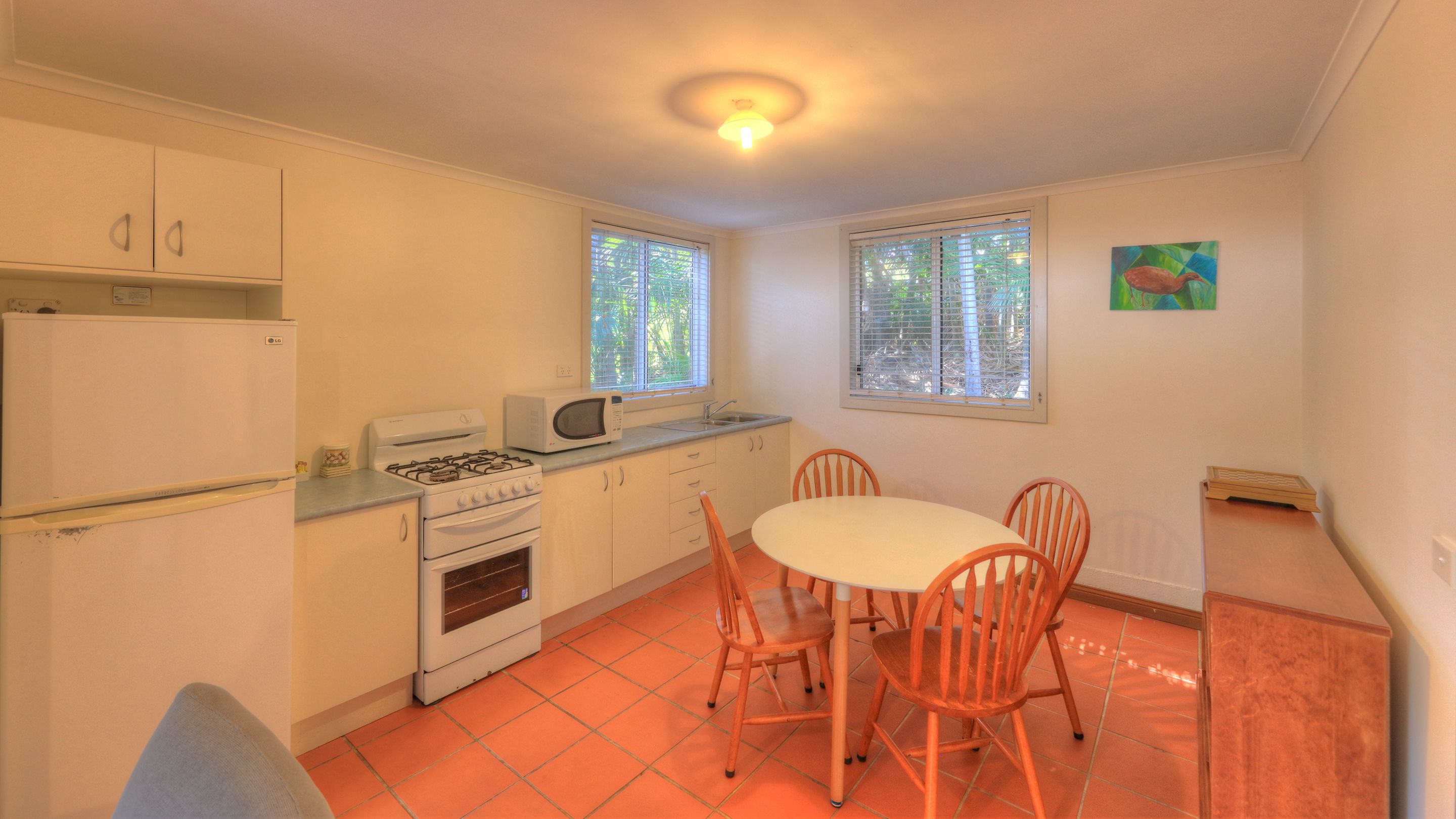 A compact kitchen with a stove, microwave, and sink, a dining table with chairs, and a window with blinds.