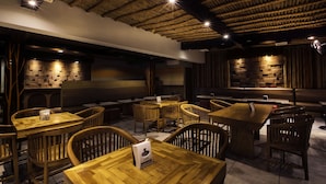 A restaurant interior with wooden tables and chairs, a brick wall, and a thatched ceiling. - Bali Bungalo Hotel (Legian)