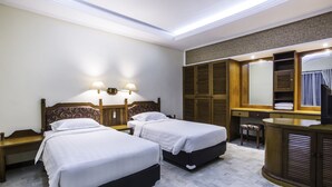 A hotel room with two beds, a desk, a chair, a vanity with a mirror, and built-in wardrobes. - Bali Bungalo Hotel (Legian)