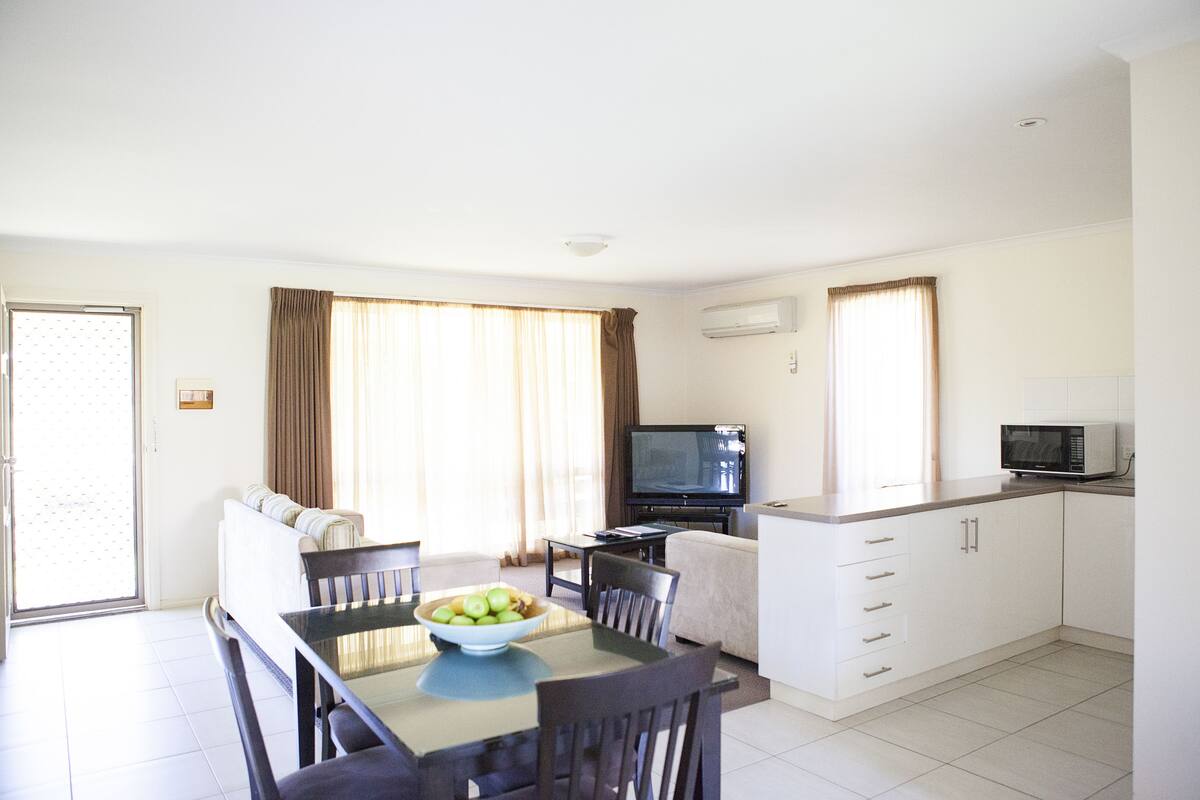 Moderni hotellihuone, jossa on ruokailutila, sohva, televisio ja pieni keittiö.
