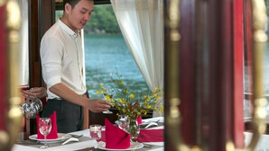 Una mesa de comedor dispuesta con servilletas rojas, copas de vino y un jarrón de flores amarillas.
