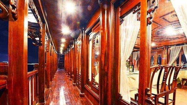 Un pasillo con columnas de madera y suelo pulido, que conduce a una habitación con una mesa y sillas.