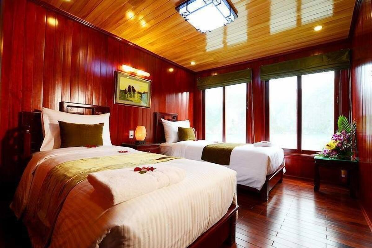A hotel room with two beds, wooden flooring, a large window, and a painting on the wall.