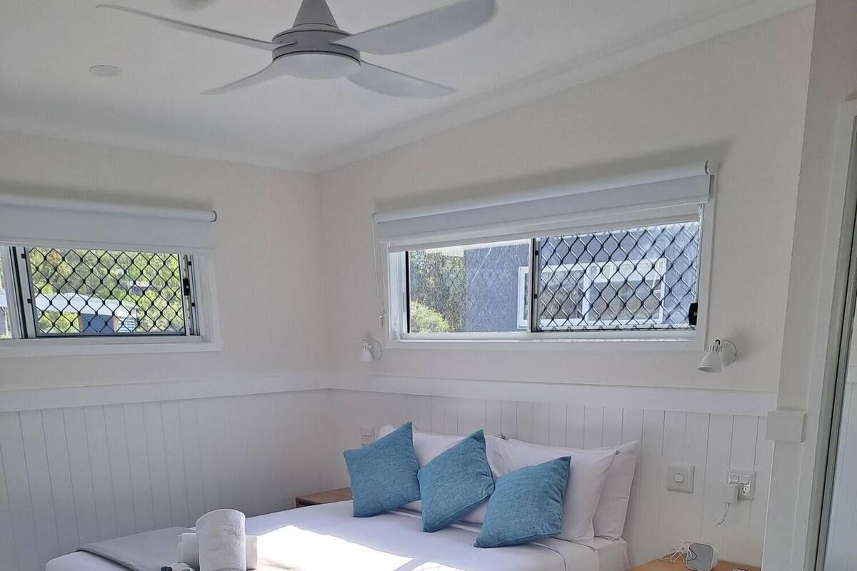 Une chambre à coucher comprenant un lit, une table de chevet, un ventilateur de plafond et des fenêtres donnant sur un paysage verdoyant.