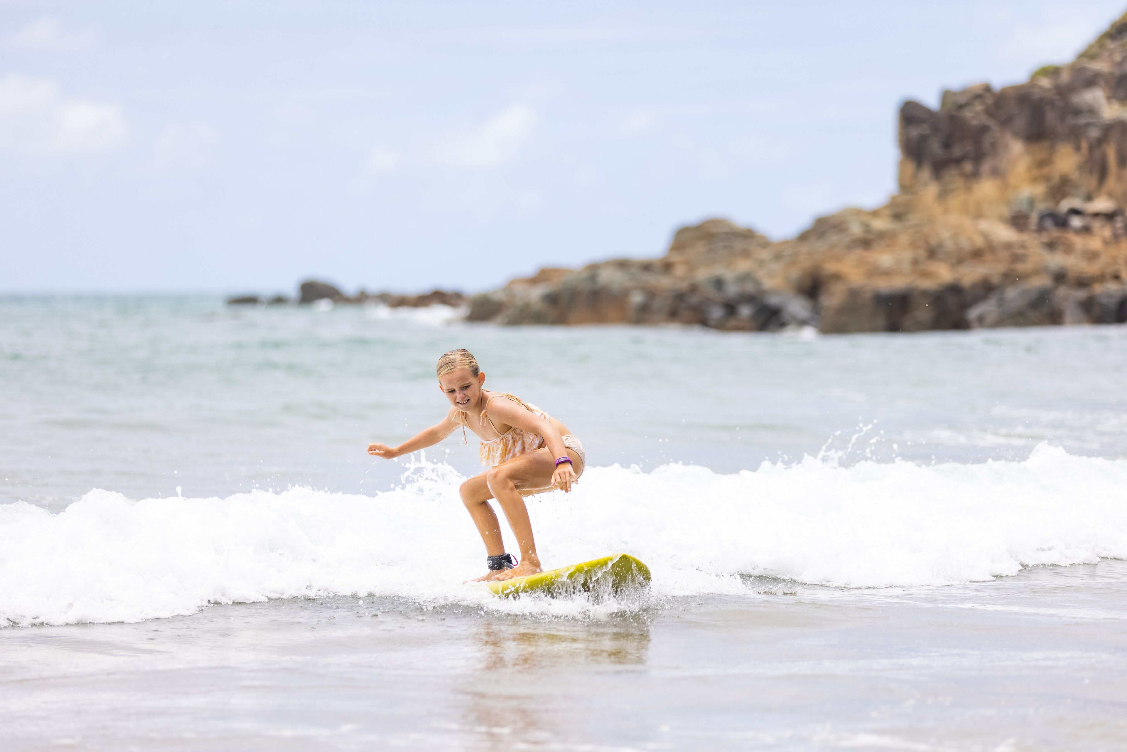 A person surfing on a yellow board at the beach with rocky cliffs in the background.