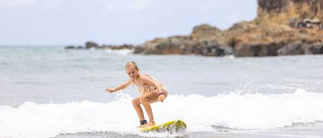 A person surfing on a yellow board at the beach with rocky cliffs in the background.