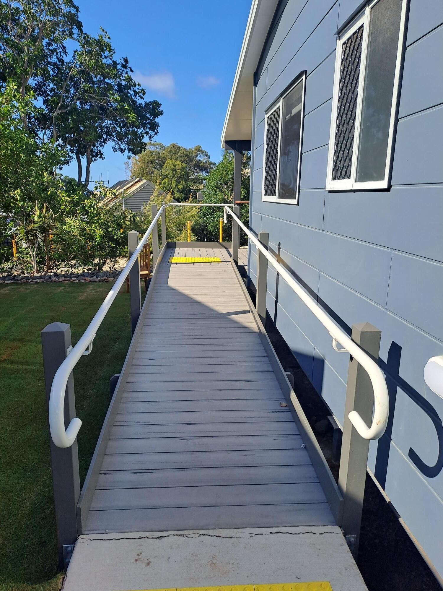 A wooden deck leading to a building with a grey exterior and white window frames.
