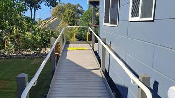 A wooden deck leading to a building with a grey exterior and white window frames.