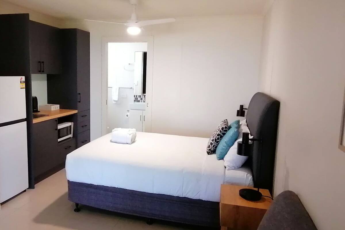 Une chambre d’hôtel de taille réduite, comprenant un lit simple, une table de chevet et un petit espace bureau avec une chaise.