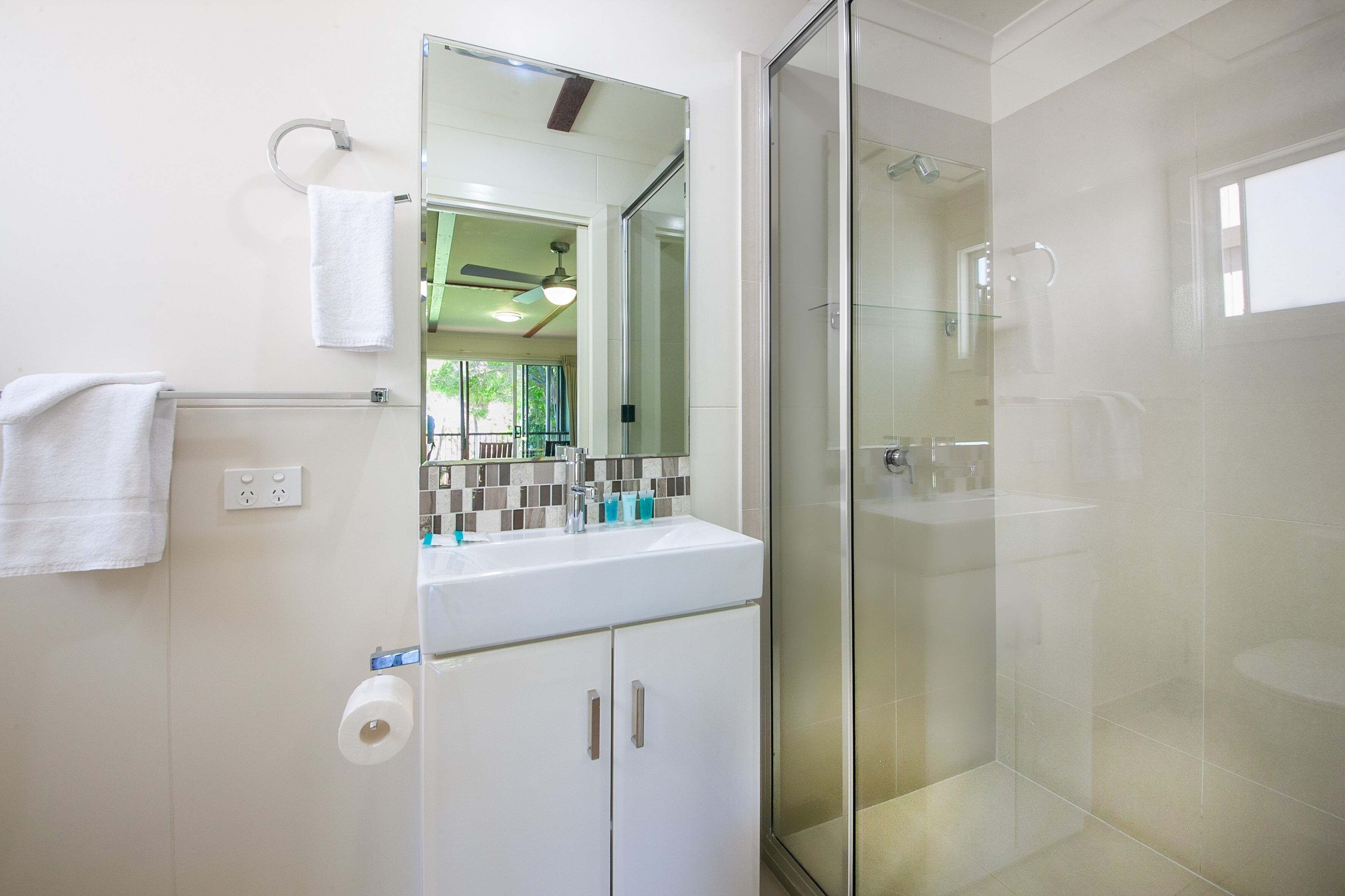 A modern bathroom with a glass shower enclosure, a white sink with a mirror above it, and a towel rack.