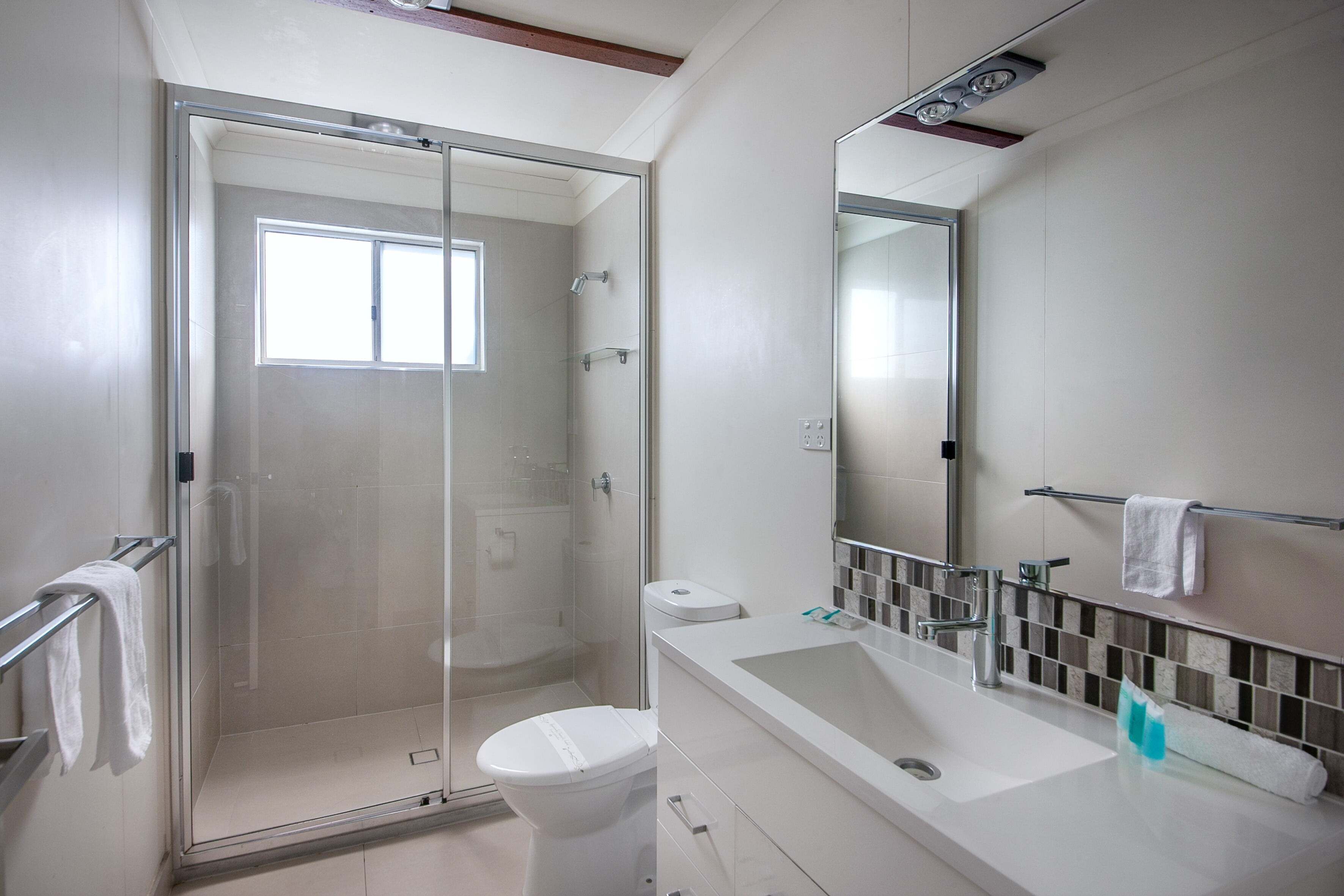 Een moderne badkamer met een douchecabine van glas, een wit toilet, een wastafel met spiegel en een handdoekhouder.