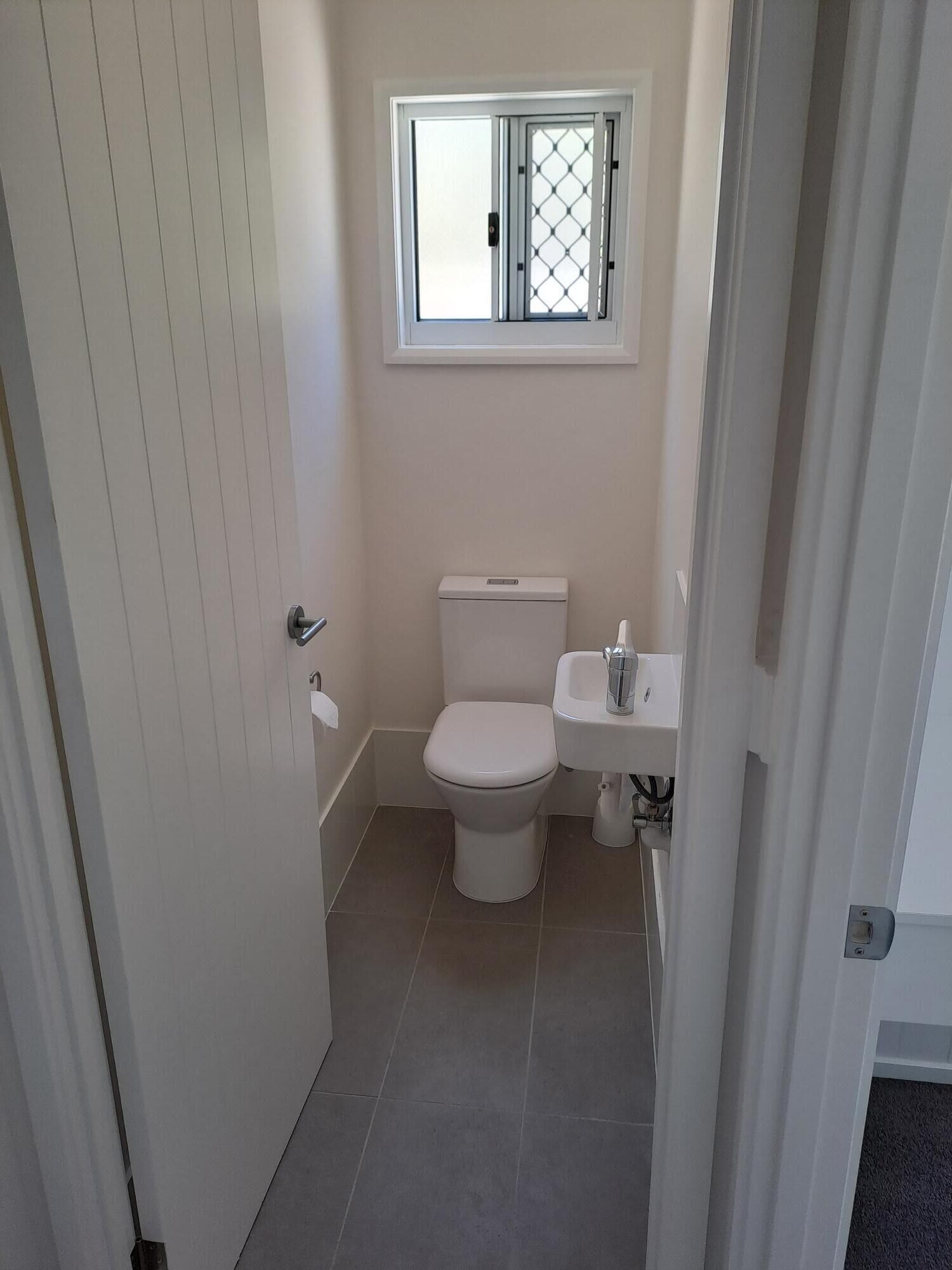 Un baño pequeño y limpio con inodoro, lavamanos y ventana sobre el inodoro.