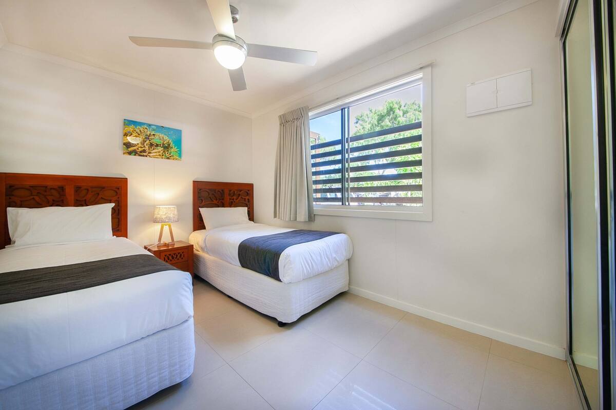 Une chambre d’hôtel avec deux lits, un ventilateur de plafond, une fenêtre avec des stores et un tableau au mur.