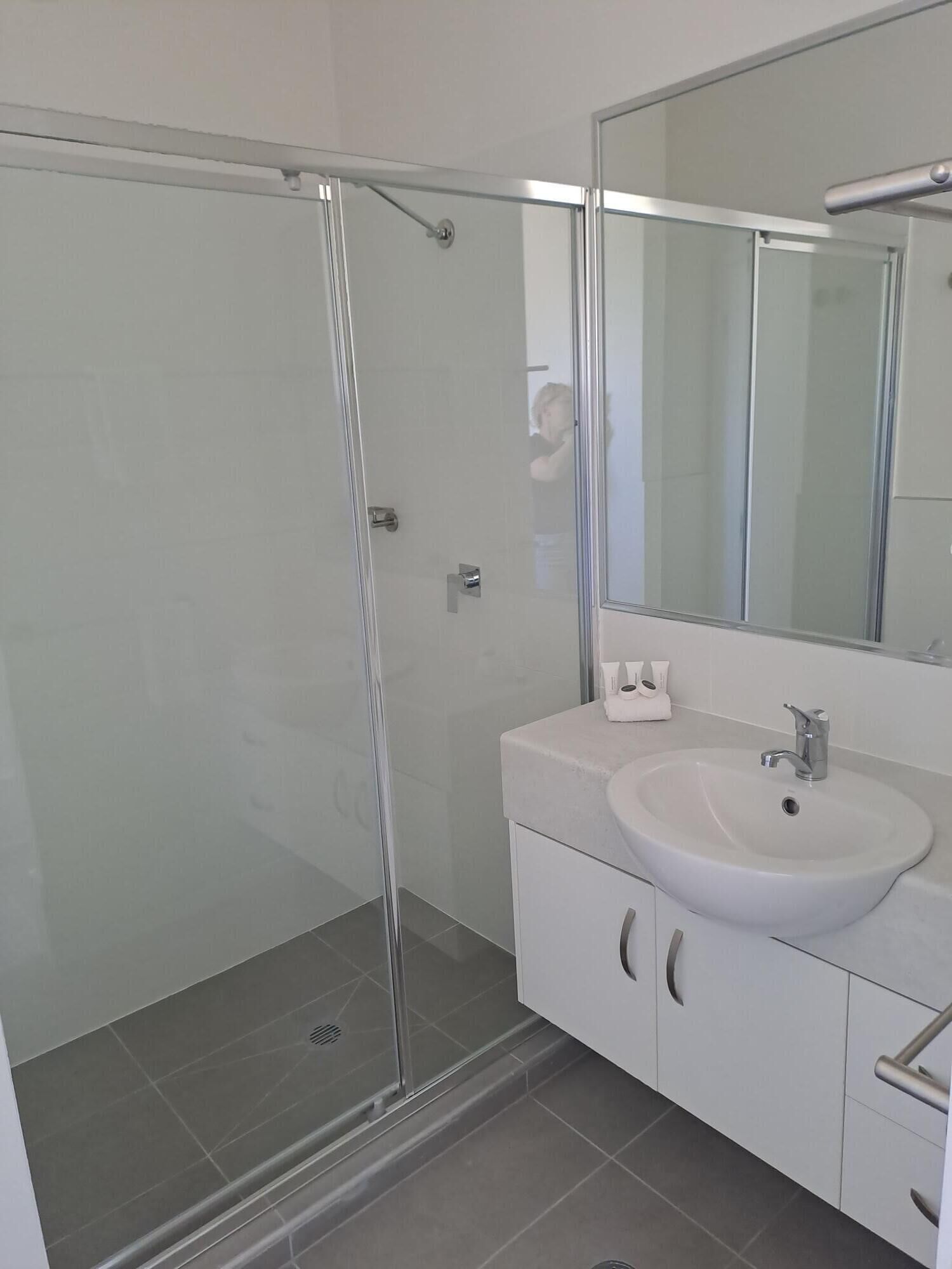 A modern bathroom with a glass shower enclosure, a white sink, and a large mirror.