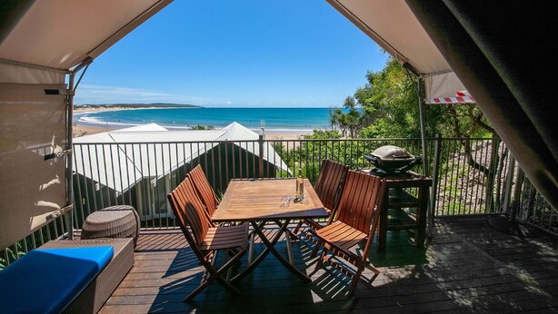 Una terraza de madera con una mesa y sillas, con vista a una playa.