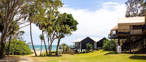 A beachfront property with a grassy lawn, a pathway leading to the beach, and a house with a balcony overlooking the ocean.