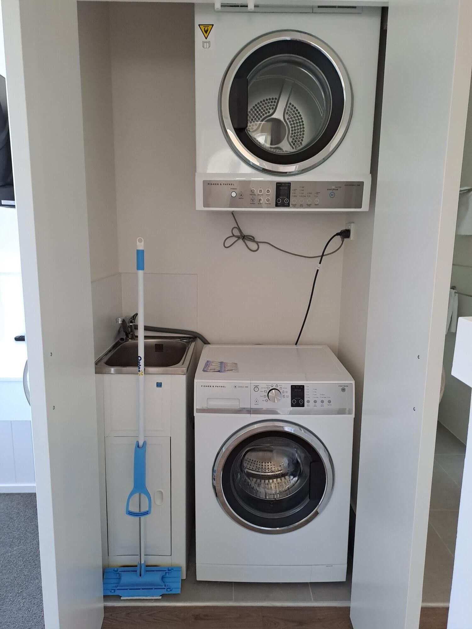 Une petite buanderie équipée d’un lave-linge et d’un sèche-linge, d’une serpillière et d’un évier.