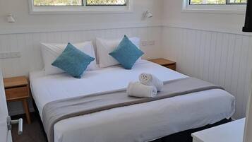 A bedroom with a bed, two bedside tables, a ceiling fan, and windows with blinds.
