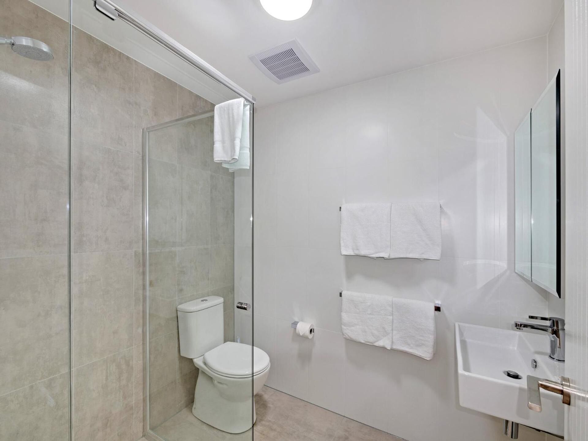 A modern bathroom with a glass shower enclosure, a toilet, a sink, and two towels hanging on the wall.