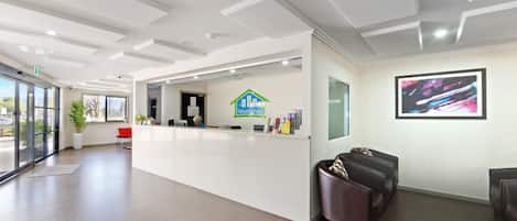 A modern hotel reception area with a white reception desk, a digital display, and a large window offering a view of the outdoors.