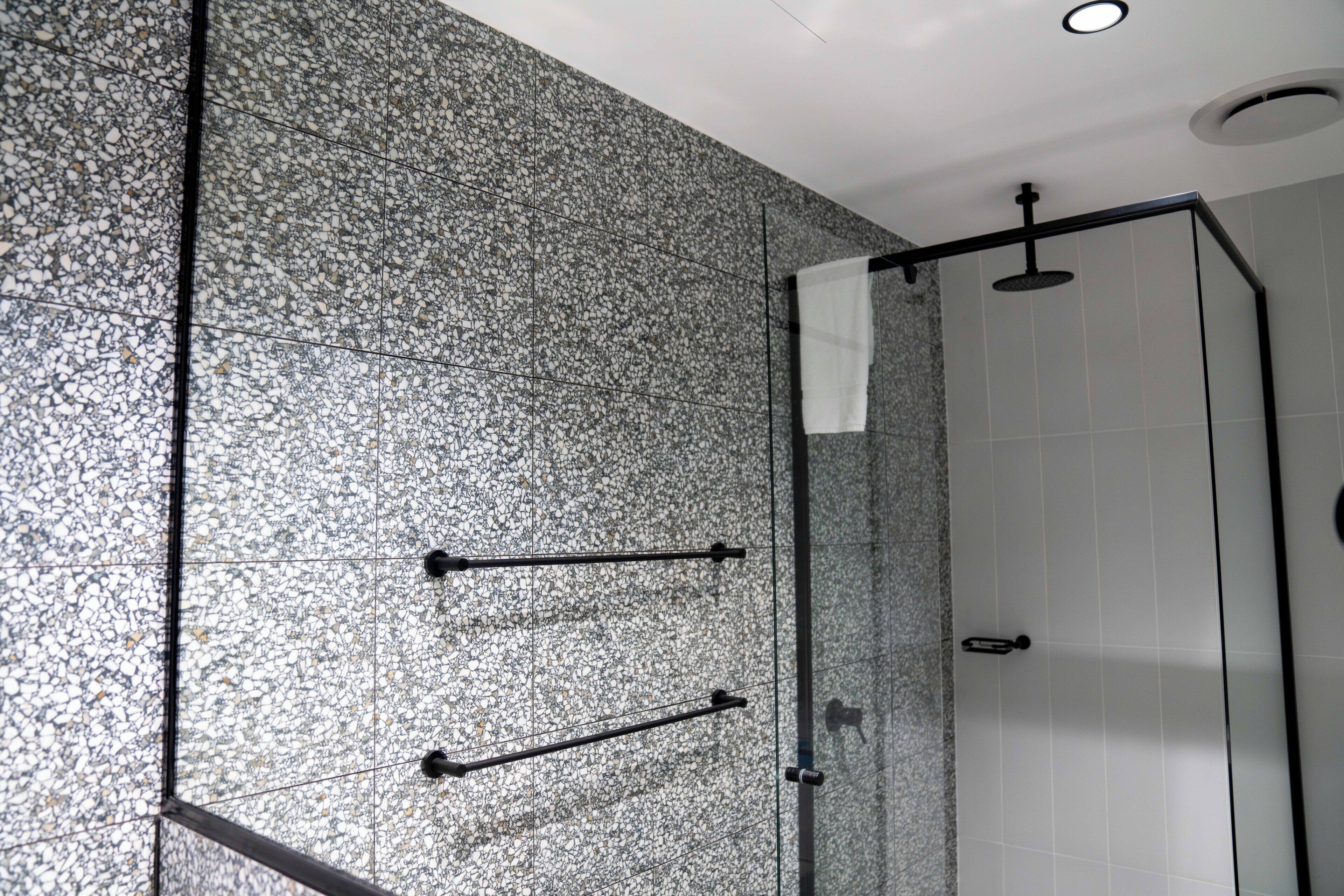 A modern bathroom with a speckled tile wall, a glass shower enclosure, and a ceiling-mounted light fixture.