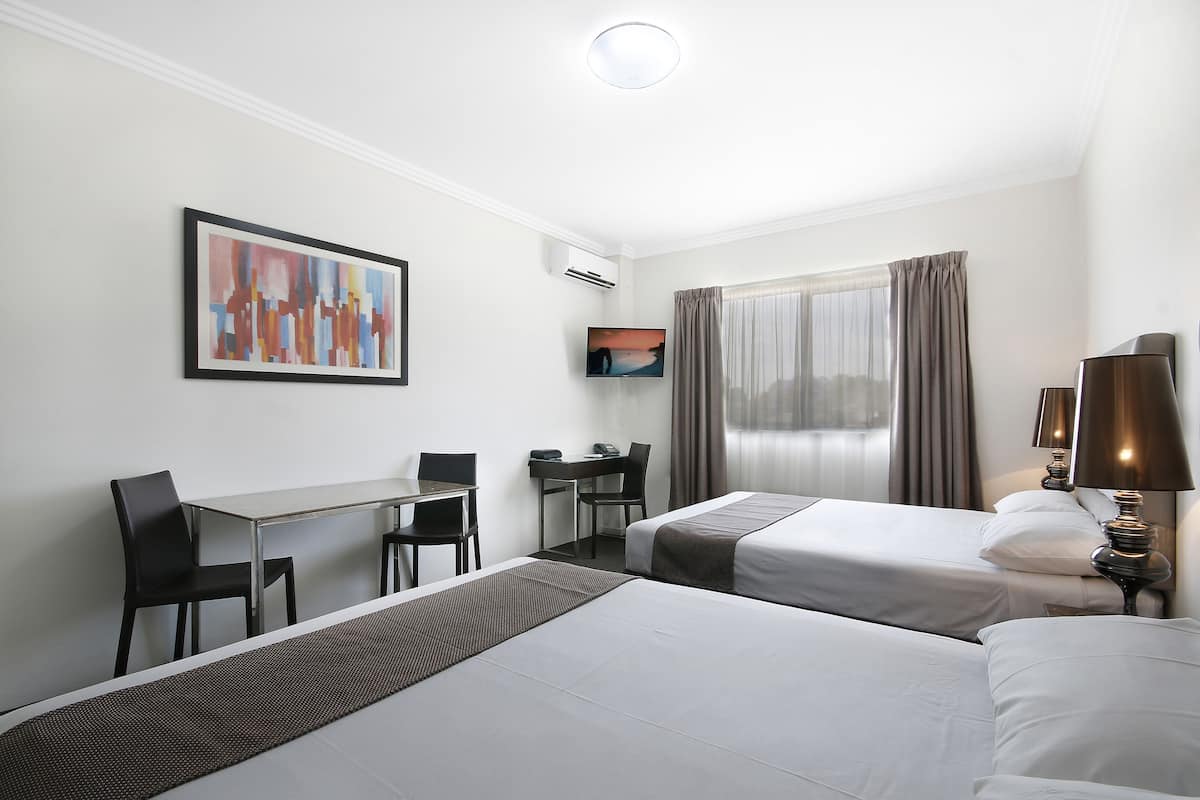 A hotel room with two beds, a desk, a chair, a TV, and a lamp.