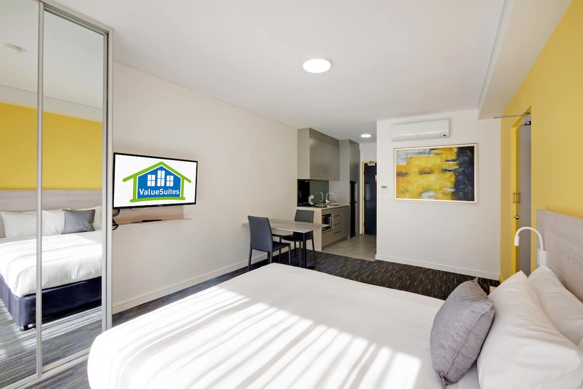 A hotel room with a bed, a desk, a chair, a TV, and a painting on the wall.