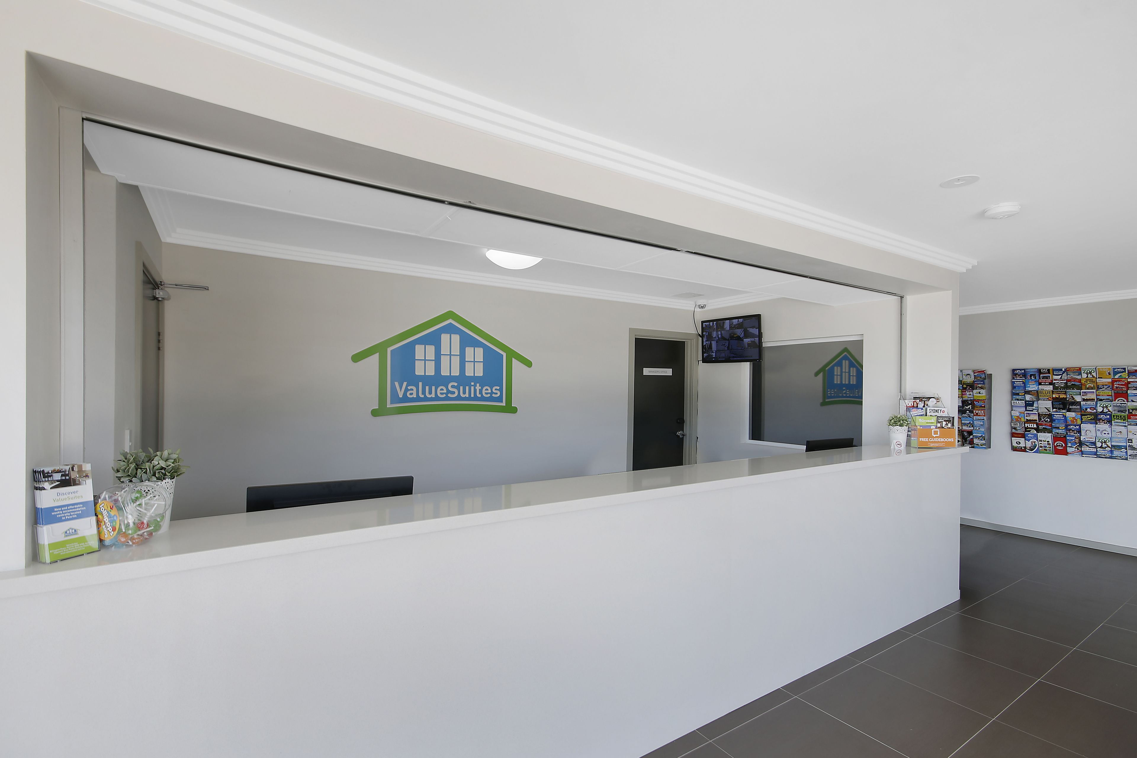 A reception area with a white counter, a green and blue house logo, a television screen, and a bulletin board with various notices.