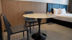 Una habitación de hotel moderna con una mesa redonda, dos sillas, una cama con ropa de cama blanca y una pared de acento de madera.