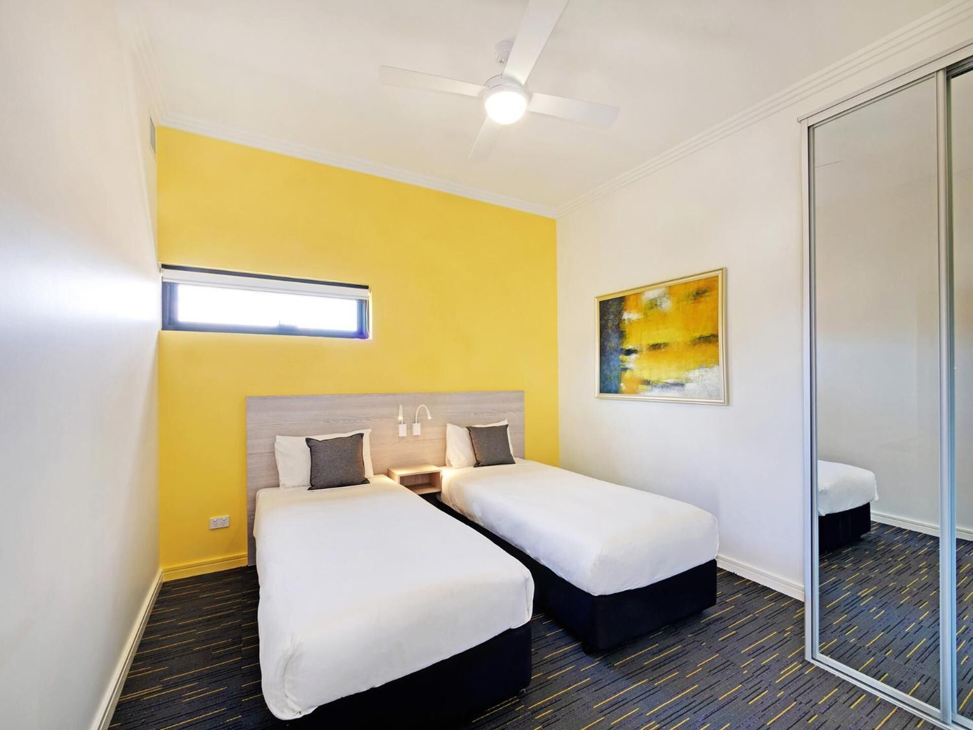 A hotel room with two beds, a ceiling fan, a window, and a painting on the wall.