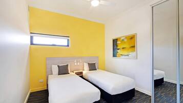 A hotel room with two beds, a ceiling fan, a window, and a painting on the wall.