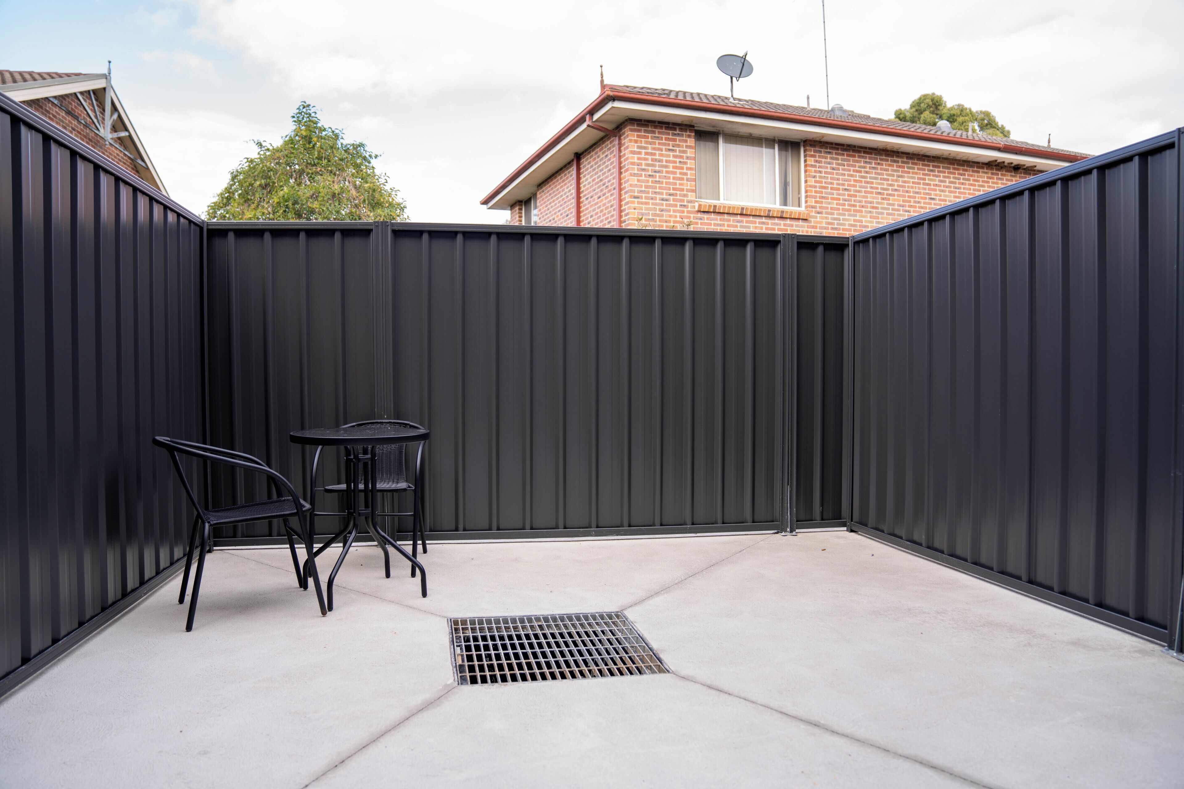 A patio with a metal fence, a metal table, and two chairs.