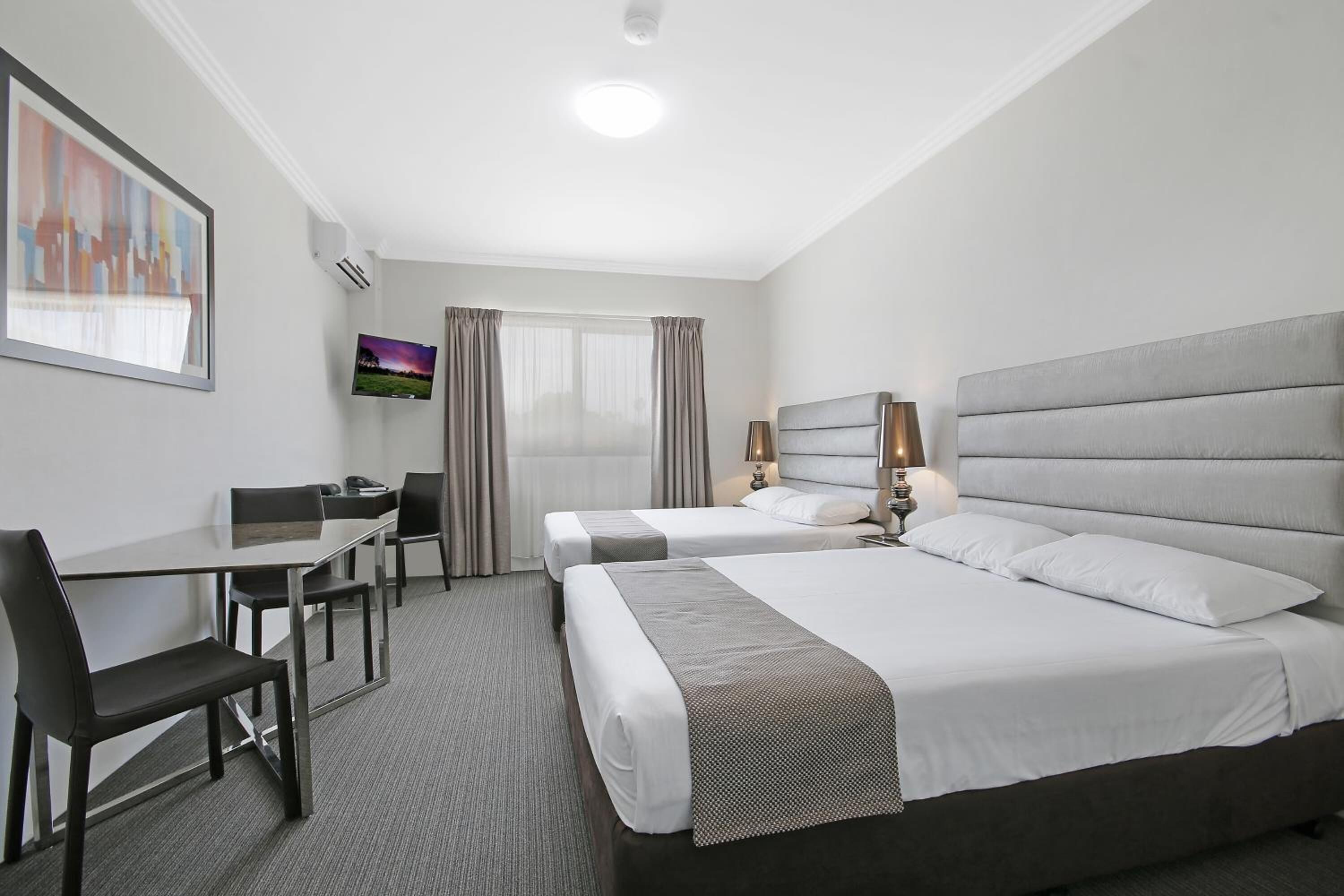 Habitación de hotel con dos camas, un escritorio, una silla y un televisor.