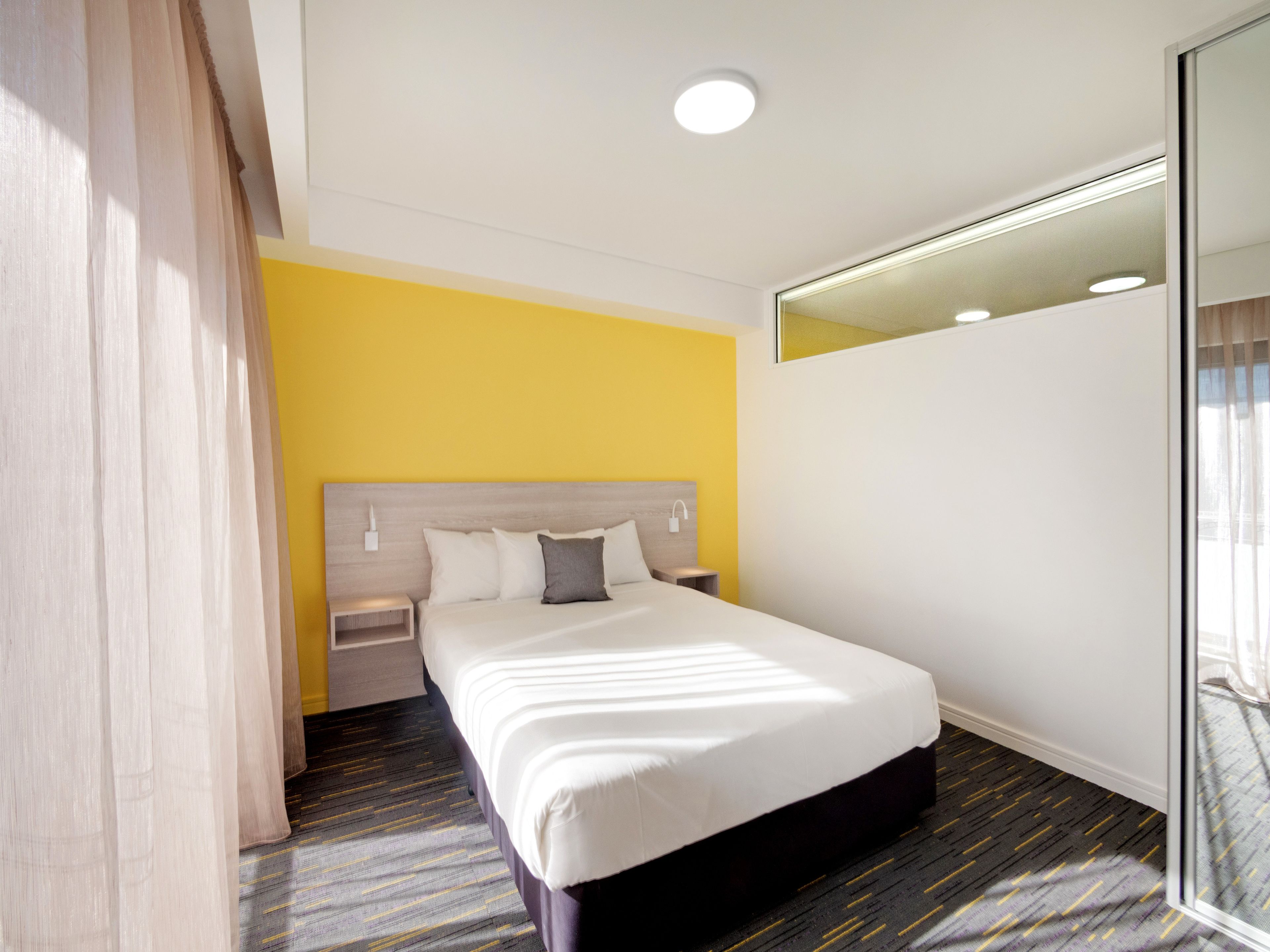 A hotel room with a bed, a nightstand, a mirror, and a window with curtains.
