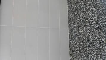 Chuveiro com um chuveiro de efeito chuva preto e parede com padrão de azulejos salpicados.