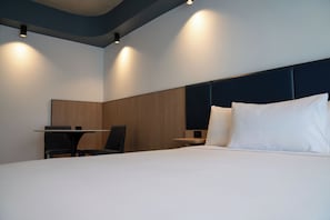 A modern hotel room with a neatly made bed, a desk, and a chair.
