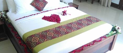 A neatly made bed with a patterned bedspread, a decorative pillow, and a heart-shaped arrangement of red flowers on the bed.