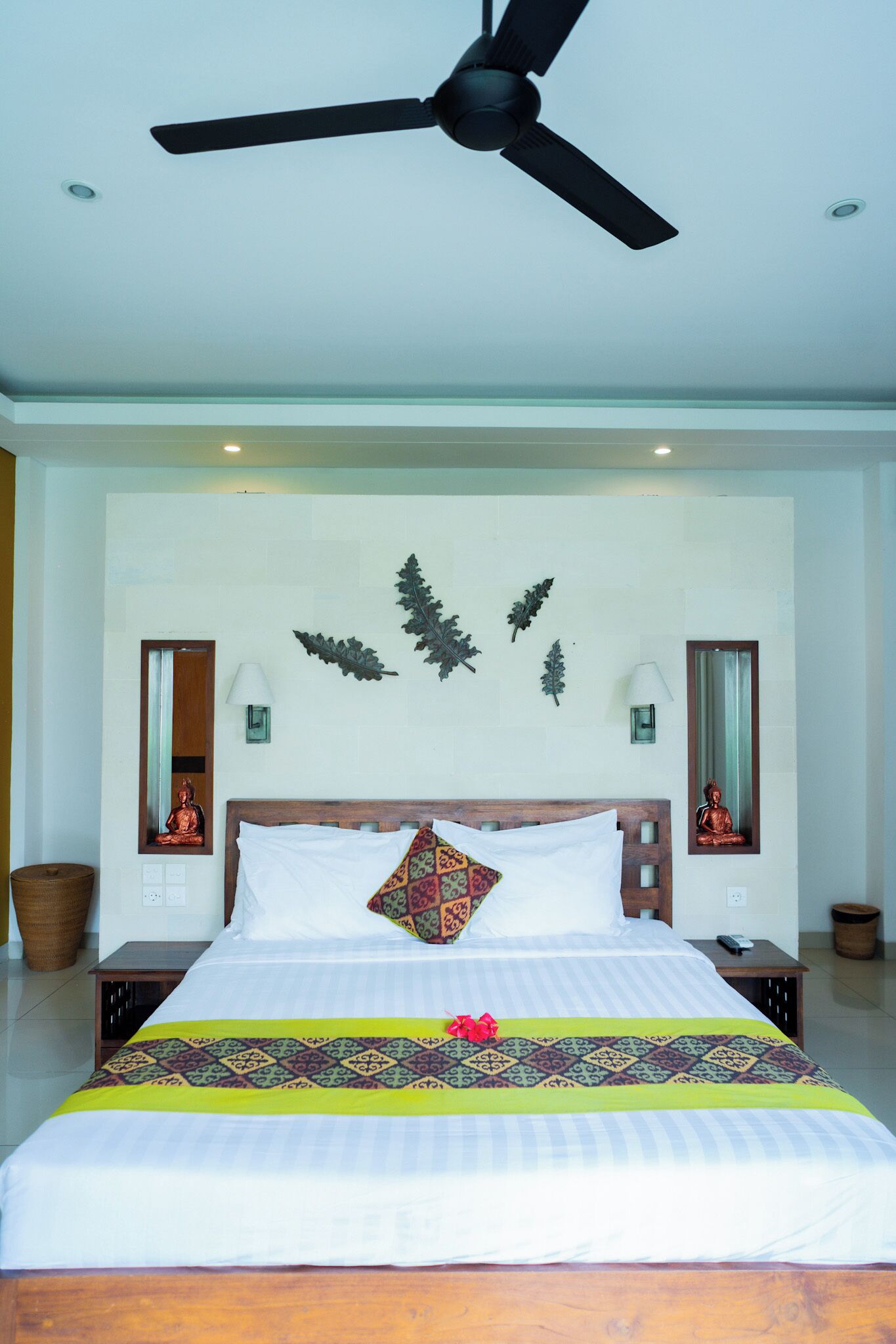 A neatly made bed with a patterned bedspread, a ceiling fan, and wall-mounted decor including leaves and statues.
