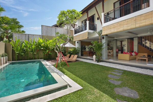 Uma casa moderna com piscina, um gramado bem cuidado e uma varanda com mobiliário de exterior.