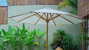 A lounge area with a curved wicker sofa, a white umbrella, and several potted plants.