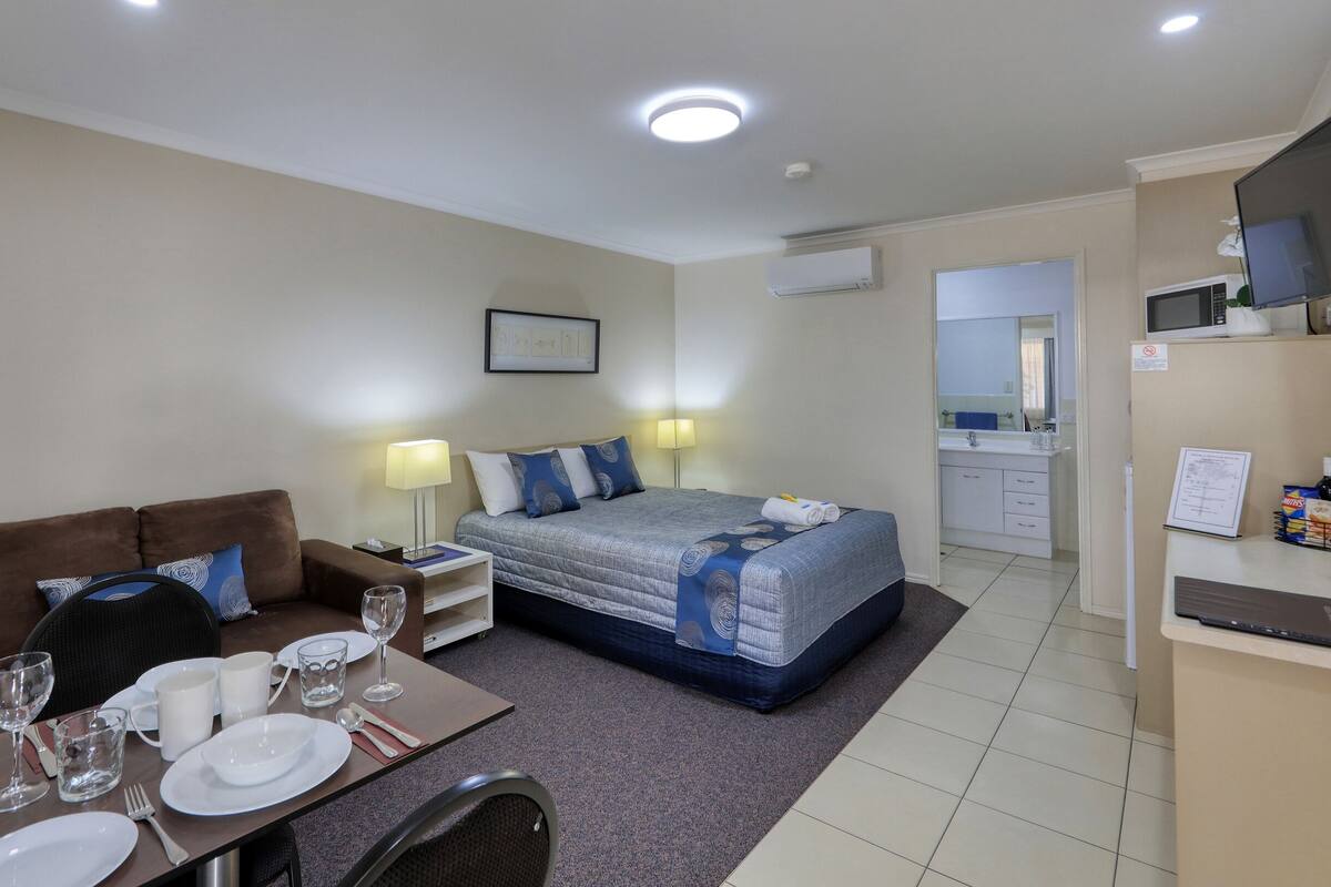 A hotel room with a bed, a sofa, a dining table with plates and glasses, a TV, and a bathroom visible through an open door.