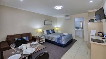 Ein Hotelzimmer mit Bett, einer Couch, einem Esstisch mit Tellern und Gläsern, einem Fernseher und einem durchgehenden Türspalt sichtbaren Badezimmer.