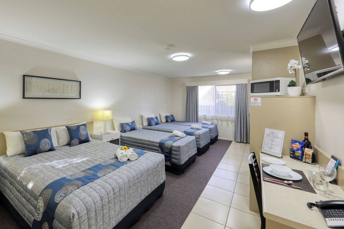A hotel room with three beds, a desk with a computer, a TV, and a microwave.